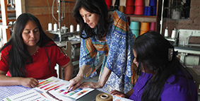 Three women working together, one pointing at a color card on a table of textiles