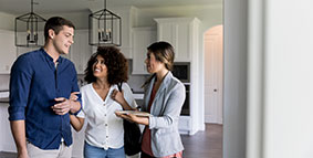 Young couple smile as they talk with a female real estate agent. The real estate agent is showing them a new home