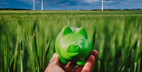 Hand holding green piggybank in a green field with wind turbines