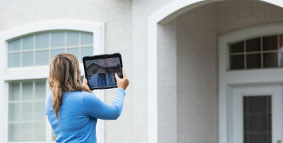 A woman standing in the front yard of a house taking photos with a digital tablet