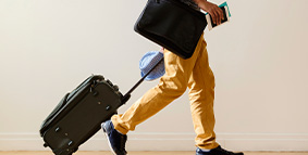 A man rolling luggage, with passport in hand as if to travel