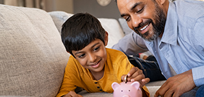 Adult with child placing coins in a piggy bank